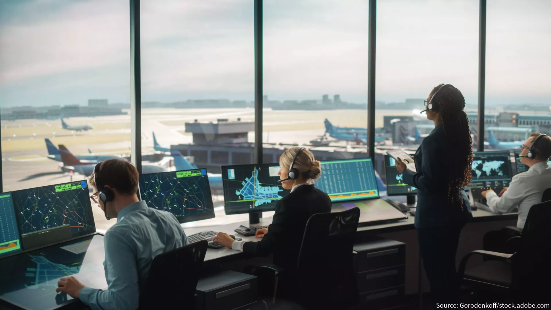 4 air traffic controllers sit in an air traffic control tower looking at screens and the runway in front of them.