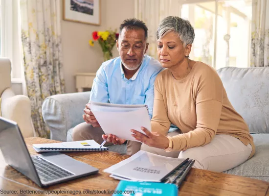 Photo showing a couple sitting on the couch while reviewing stacks of financial documents together.