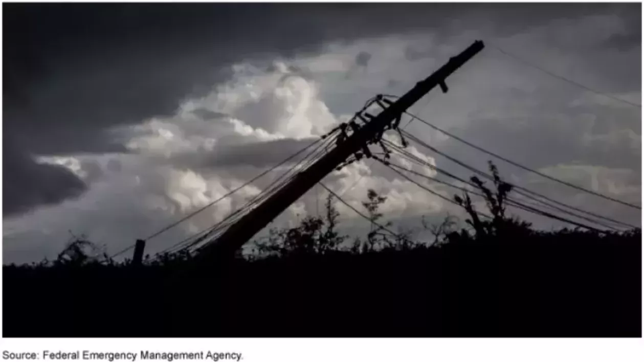 Image shows a downed powerline pole silhouetted against a stormy sky.