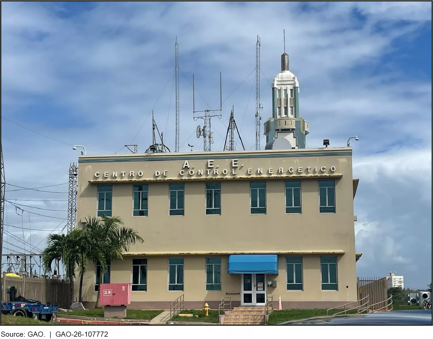 Image of the Monacillos Primary Control Center in San Juan, Puerto Rico, February 2025. It is a tan colored building with some palm trees out front an and array of antennas on its roof.