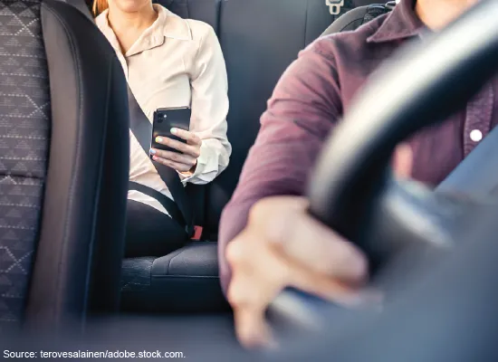 A person using their cell phone in the back seat while somebody else drives.