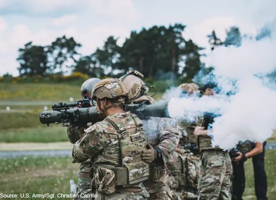 A service member holding a blast weapon as other service members stand nearby.