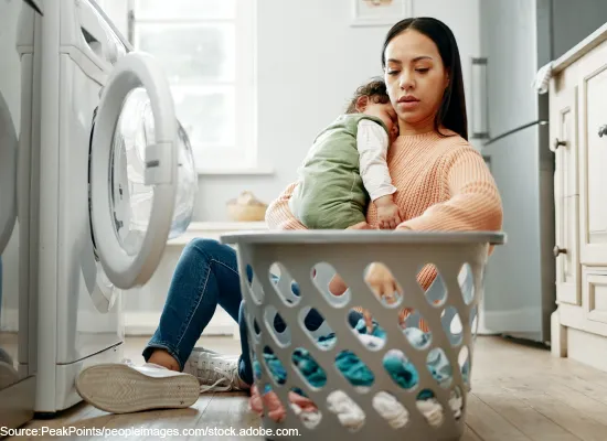 A woman doing laundry while holding a child.