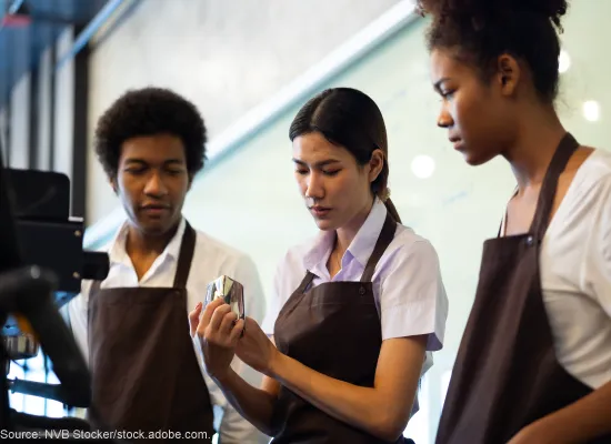 Teenage workers learning how to work an espresso machine.