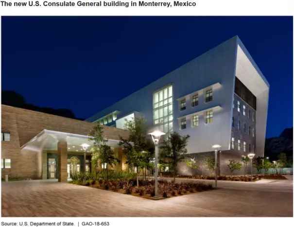 Picture of a modern building with a brick entryway at night with lights and plantings.