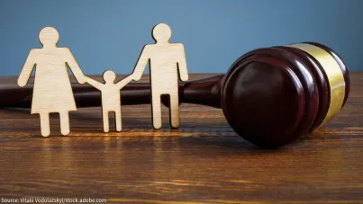 Image shows wooden silhouettes cut out in the shape of a family with a mother and father holding a childs hands. Next to them sits a gavel.