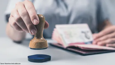 Image shows someone inking a stamp with one hand and holding a passport ready to stamp in the other.