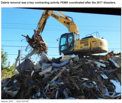 Photo of a large yellow excavator on top of a pile of debris emptying its bucket