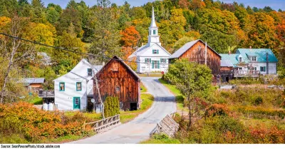 Photo showing a rural town country road in Fall. Orange and gold leaves with a white chapel in the background.