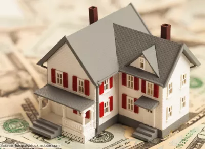 Stock image showing a toy house sitting on a pile of money.
