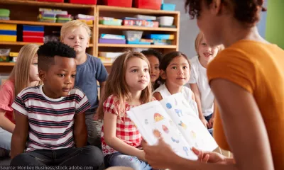 A teacher reads to a class of young children as they sit on the floor.