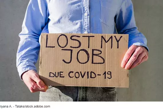 Photo (staged) of a man holding a cardboard sign that says he lost his job due to COVID-19