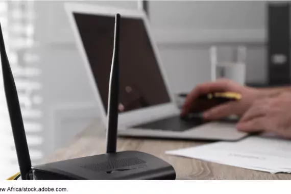 Photo showing a person working at their desk on a laptop with a WIFI router in the foreground