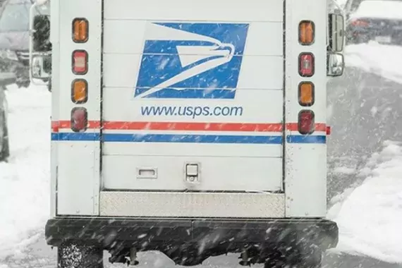 Photo showing a U.S. Postal Service delivery vehicle driving through a snow covered road.
