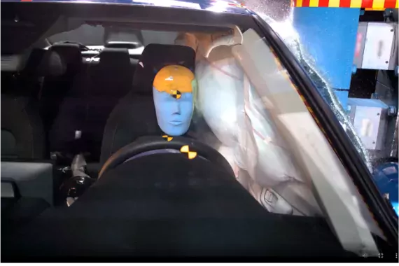 Photo showing a crash dummy behind the steering wheel of a car with the side air bag filled.