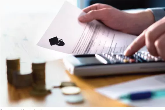 Photo showing a hands on a desk. One hand is holding a financial aid offer (piece of paper). The other hand is on a calculator adding up expenses.