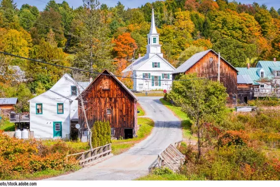 Photo showing a rural town country road in Fall. Orange and gold leaves with a white chapel in the background.