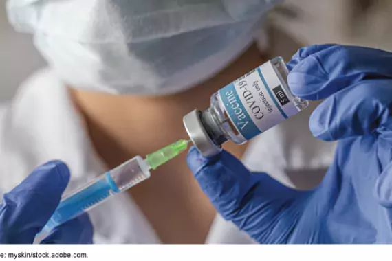 Photo showing a medical worker with a mask on filling a shot syringe with COVID-19 vaccine.