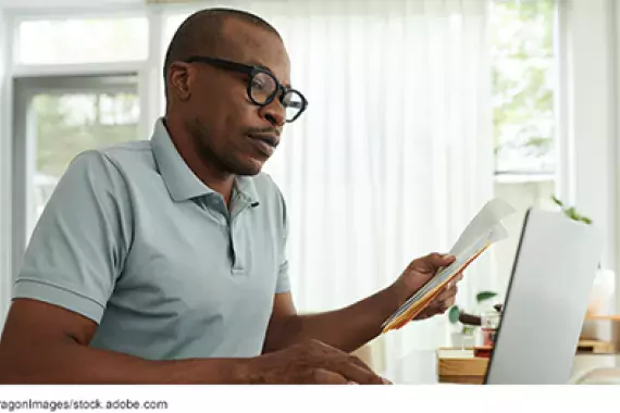 a man looking at paperwork in front of a laptop