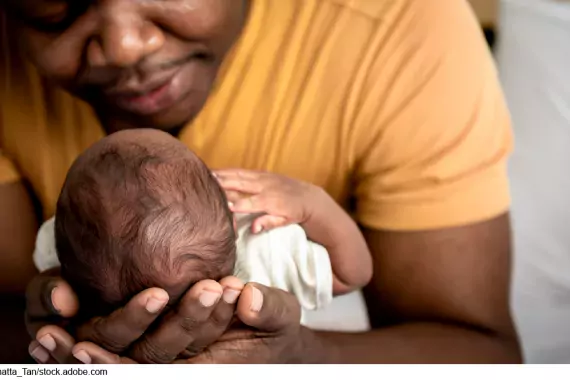 Photo showing a father cradling a new born baby in his arms.