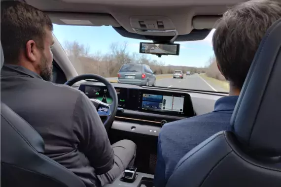 Stock image showing a driver and passenger in the front seat of a car using driver assisted technologies.