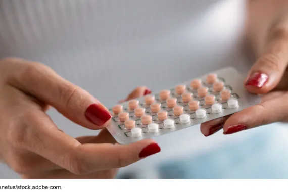 Close up of a person's hands with painted red fingernails holding a pack of oral contraceptives
