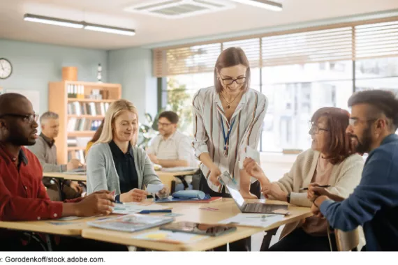 A group of people in a classroom talking while sitting in groups.