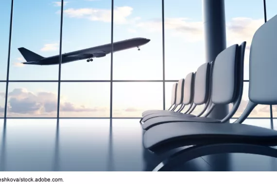A flying airplane viewed from the window of an airport seating area. 