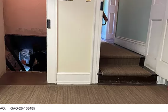 A photograph taken inside a museum in a historic house, showing a doorway leading to a hallway 2 steps up and another doorway to a basement. 