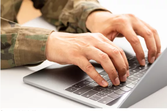 A person in military fatigues typing on a computer.