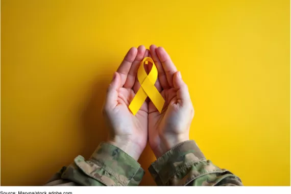 Hands from a person wearing a military uniform hold a yellow ribbon, symbolizing hope and military support.  