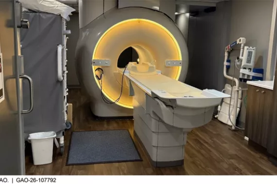 An MRI machine, which looks like a medical exam table positioned at the opening of a large plastic cylinder with a hole large enough for the exam table to enter.