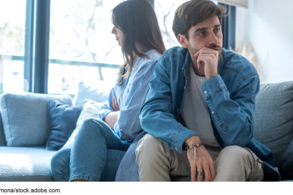 Couple sitting back-to-back on a sofa.