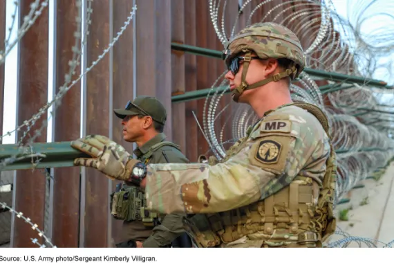 U.S. Army solider and Border Patrol agent stand at border wall