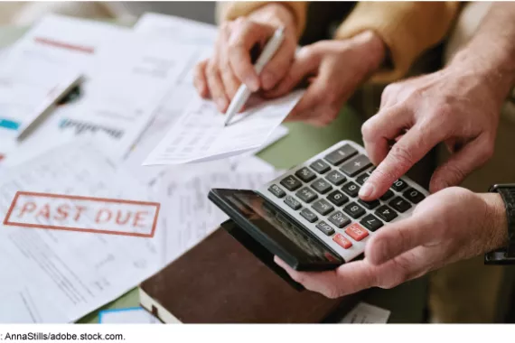 One person's hands hold a calculator, while another's hold a bill and a pen. A notice of a past due payment is on the table next to them.