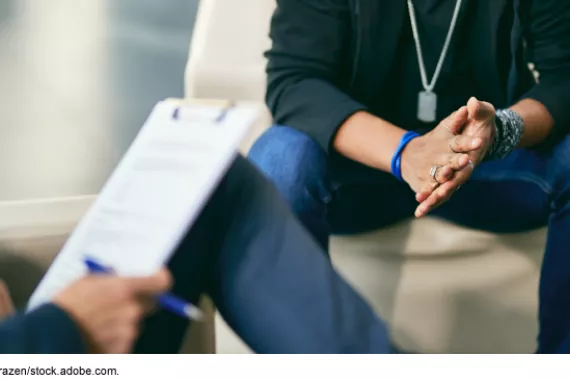 A person wearing military dog tag seated across from a person with a clipboard.