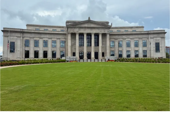 A large, two story stone building with columns at the main entrance with a green lawn in front.
