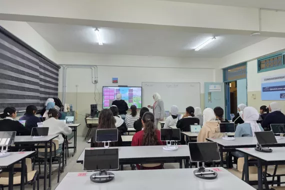 Teachers provide a lesson on an electronic board to a classroom full of Palestinian students. 