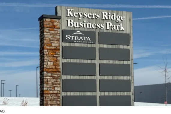 A business park sign made of brick and wood with 10 placards for business names in a snowy field. 