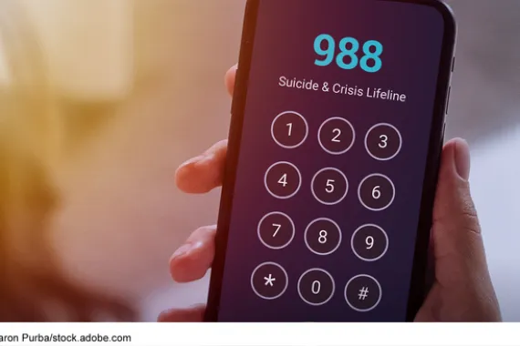 Hand holding a mobile phone with the 988 Suicide & Crisis Lifeline on the screen.