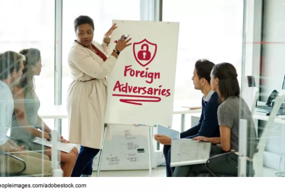 A group of people in a business setting with one person standing next to a poster board that says Foreign Adversaries.