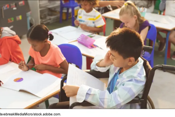 Kids studying in the classroom with one child sitting in a wheelchair reading.