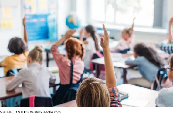 Students raising their hands in a classroom.