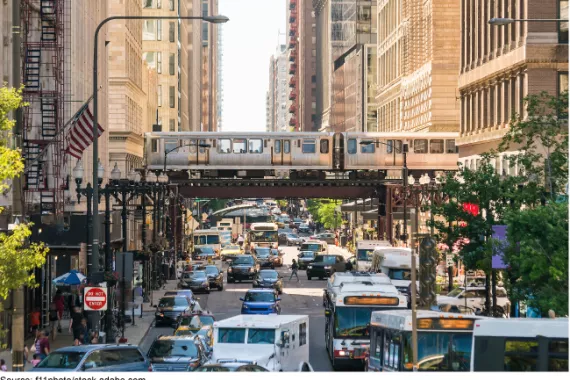 A downtown cityscape with tall buildings, rail transit, cars, and people.