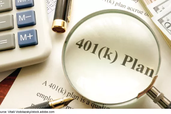 Magnifying glass focused on the words 401(k) Plan. Desktop items, including a calculator, pens, and paper.
