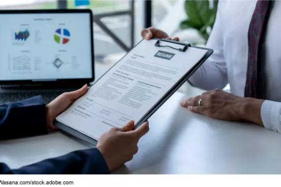 A person holding a resume in front of a computer. 
