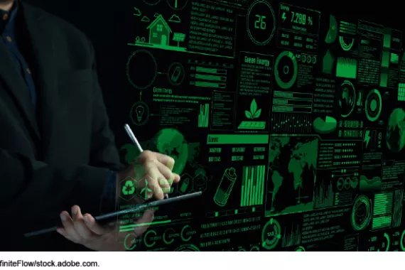 A person writing on a tablet in the background with a digital dashboard projection from the laptop of schematics, data, and numbers related to finances and renewable energy
