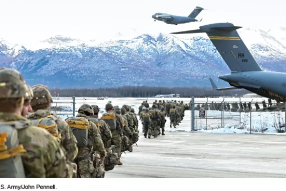 Army paratroopers lining up to board a large transport aircraft in front of snowy mountains.