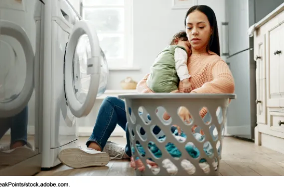 A woman holding a baby sitting on the floor doing laundry