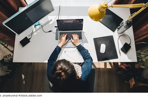 A female employee is working on a laptop and monitor at her desk at home.